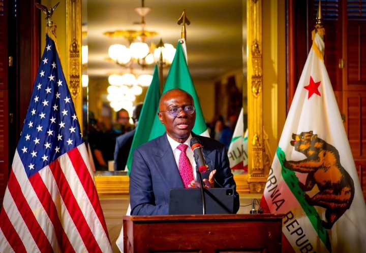 Sanwo-Olu in a suit, on a podium with the flag of the United States, Nigeria and the state of California behind him