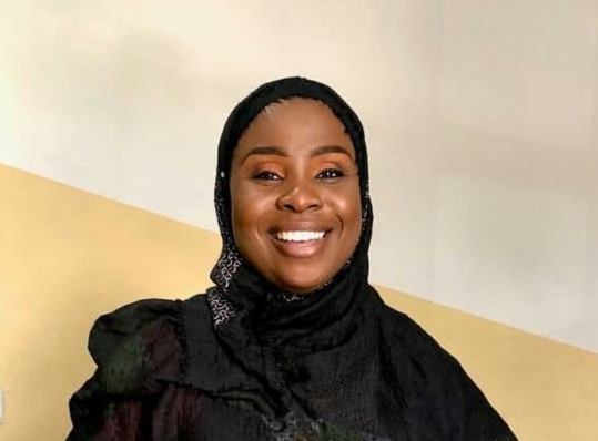 Nyma Akashat in a black hijab, smiling against a two coloured wall.
