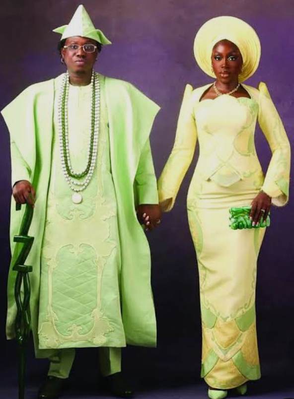 Zlatan Mobile in a royal inspired Agbada, holding a customized walking stick, while holding hands with DaVita, who is dressed in a royal inspired iron, Buba and gele.